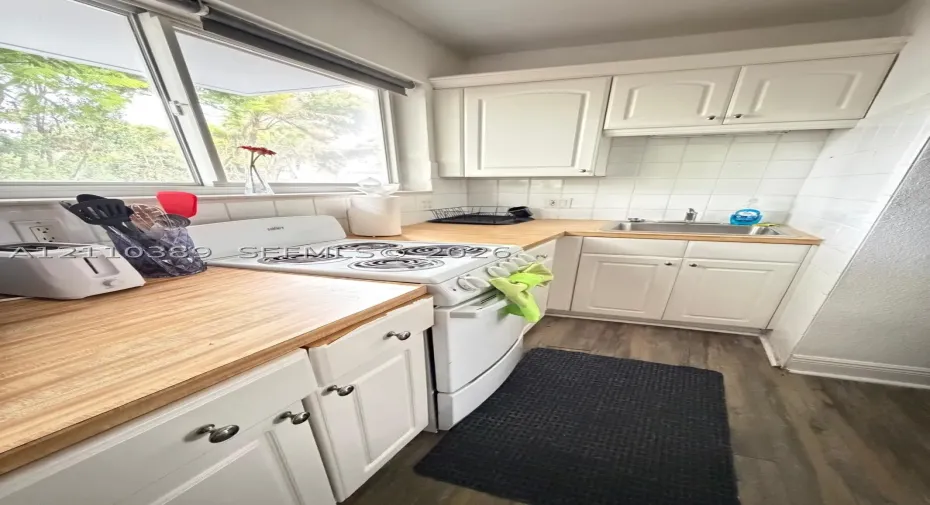 Kitchen featuring white cabinetry, butcher block countertops, wood-finish flooring, a stainless steel sink, and white ceramic tile backsplash