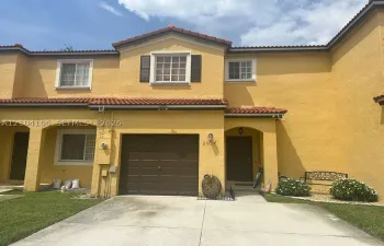 Stucco exterior featuring a terra cotta tile roof, recessed entryway, attached garage, and divided-lite windows with dark shutters