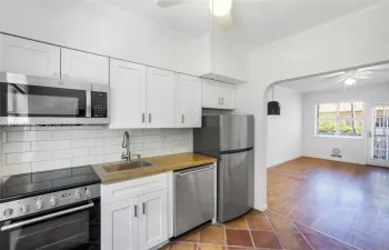 Kitchen featuring white Shaker-style cabinetry, stainless steel appliances, a white subway tile backsplash, a wood-finish countertop, and terracotta tile flooring