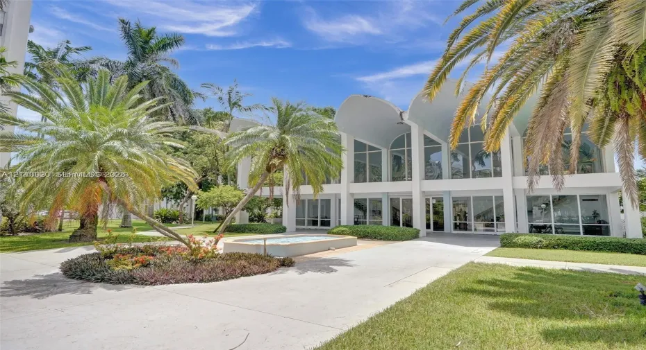 Mid-century modern exterior featuring dramatic vaulted rooflines, expansive floor-to-ceiling glass windows, concrete hardscaping, and established palm landscaping