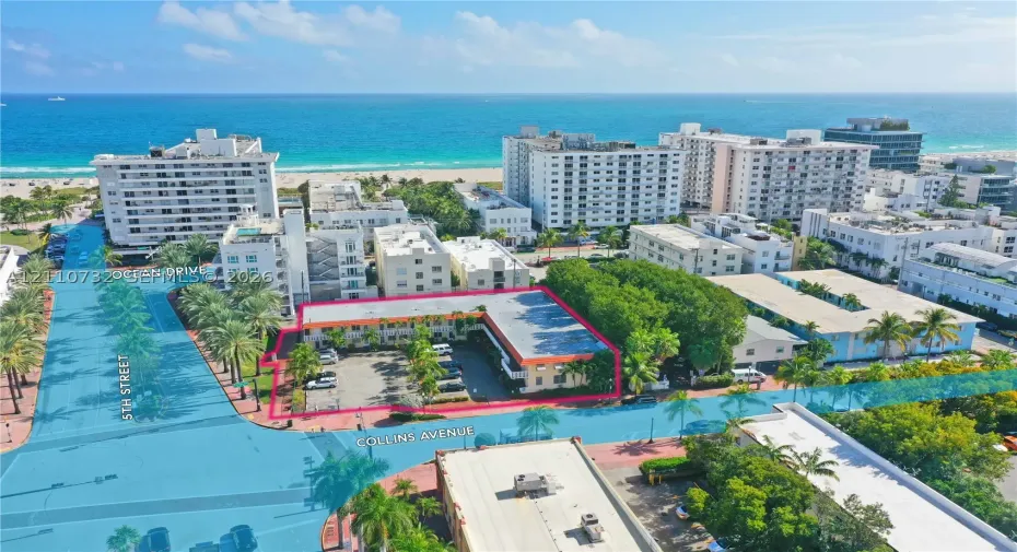Aerial perspective of a multi-story property featuring a flat roofline, an asphalt parking lot, and mature palm trees located near the intersection of 5th Street and Collins Avenue