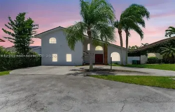 Two-story residence featuring white stucco exterior, arched windows, dual palm trees, and a concrete driveway