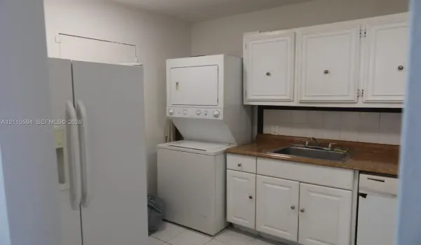 Laundry area featuring stacked laundry appliances, white cabinetry, a stone-finish countertop, and a stainless steel drop-in sink