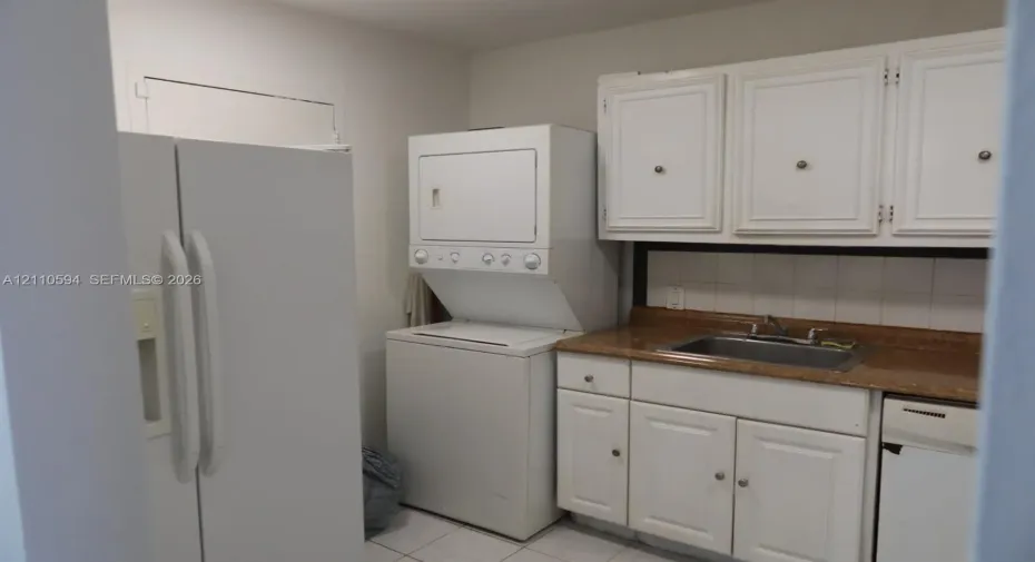 Laundry area featuring stacked laundry appliances, white cabinetry, a stone-finish countertop, and a stainless steel drop-in sink