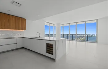 Kitchen featuring flat-panel cabinetry, a stone-surfaced island with an integrated wine refrigerator, large-format tile flooring, and floor-to-ceiling windows