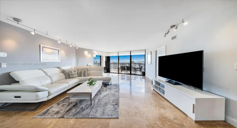 Living space featuring polished stone flooring, floor-to-ceiling glass sliding doors, track lighting, and a painted accent wall