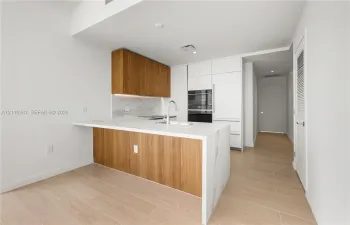 Kitchen featuring wood-finish cabinetry, waterfall-edge countertop, integrated appliance suite, and wood-finish flooring