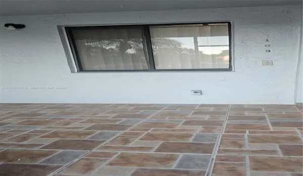 Covered exterior entryway featuring textured white stucco walls, multi-tonal decorative tile flooring, and a single-pane sliding window