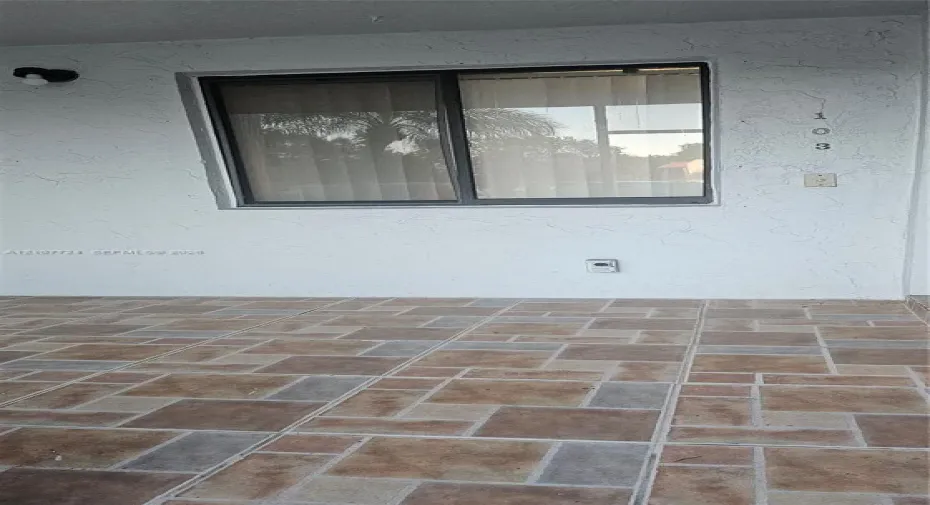 Covered exterior entryway featuring textured white stucco walls, multi-tonal decorative tile flooring, and a single-pane sliding window