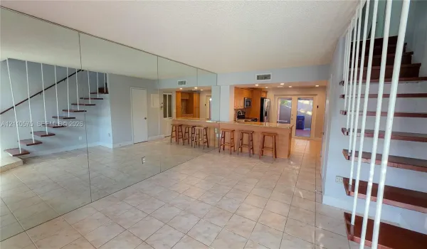 Open-concept space featuring tile flooring, a mirrored wall, a kitchen peninsula with bar seating, and floating-style stairs with white metal railings
