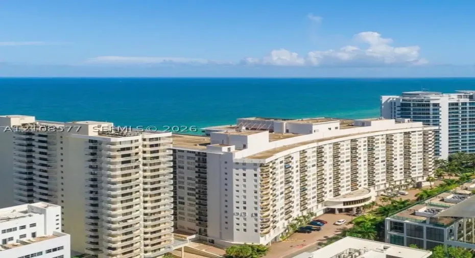 High-rise coastal development featuring white concrete facade, stacked private balconies, and expansive water frontage