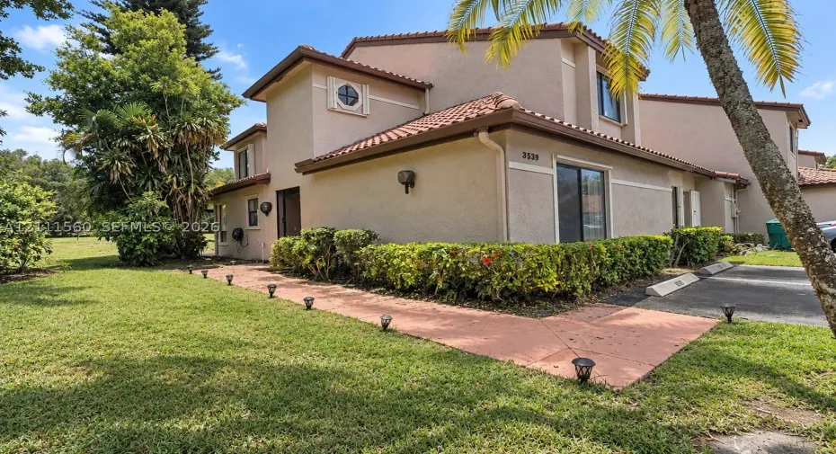 Stucco exterior with a tiled roof, multi-level architectural design, circular accent window, concrete walkway, and landscaped shrubbery