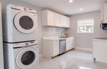 Utility space featuring white shaker-style cabinetry, stone-finish countertops, tile backsplash, stainless steel dishwasher, and large-format porcelain tile flooring