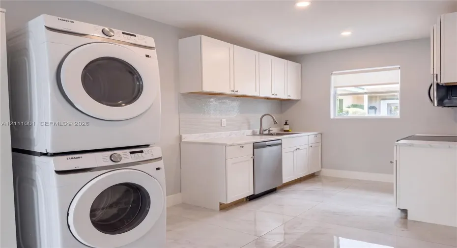 Utility space featuring white shaker-style cabinetry, stone-finish countertops, tile backsplash, stainless steel dishwasher, and large-format porcelain tile flooring