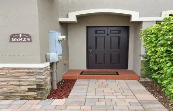 Entryway featuring a four-panel door, arched architectural detailing, natural stone veneer base, tiled porch, and paved walkway.