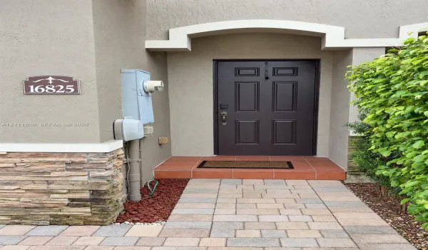 Entryway featuring a four-panel door, arched architectural detailing, natural stone veneer base, tiled porch, and paved walkway.