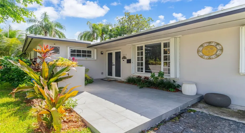 Covered entryway featuring large-format tile flooring, double-door entry, and windows with grid detailing