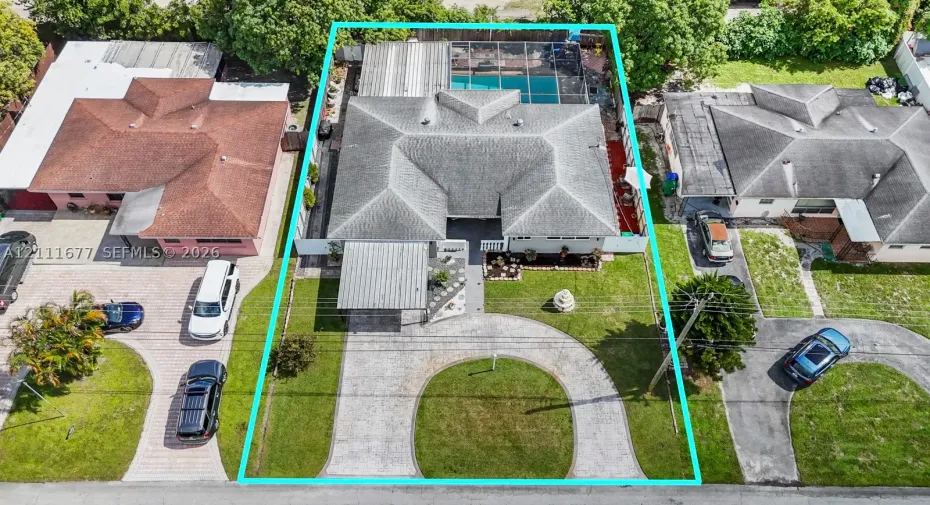 Aerial perspective of a property featuring a circular paver driveway, a front-facing covered carport, a hip roof, and a screened-in rear pool enclosure