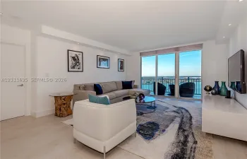 Living area featuring light-toned flooring, recessed ceiling lighting, and floor-to-ceiling glass panel doors opening to a balcony with metal railings