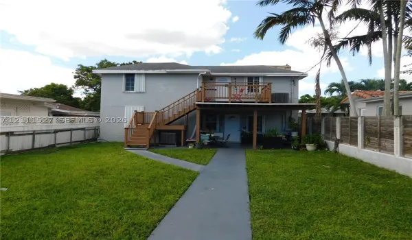 Two-story exterior featuring a wood-deck balcony, external staircase, covered ground-level patio, and fenced-in lawn area