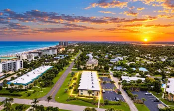 Aerial perspective of the coastal property featuring paved on-site parking, exterior lighting, and immediate proximity to the shoreline