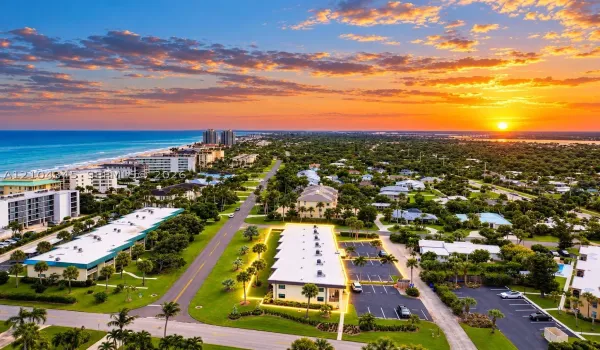 Aerial perspective of the coastal property featuring paved on-site parking, exterior lighting, and immediate proximity to the shoreline