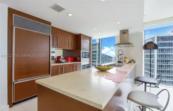 Kitchen featuring wood-finish cabinetry, an integrated refrigerator, a stone countertop island, stainless steel range hood, and floor-to-ceiling windows