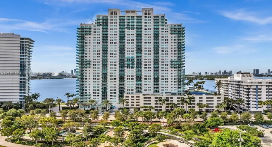 High-rise building with multiple balconies, a rooftop pool, and surrounding green spaces