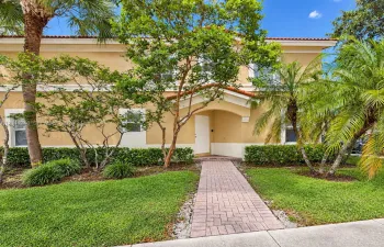 Two-story stucco exterior with a tiled roof, covered entryway, and stone paver walkway surrounded by mature landscaping