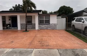 Exterior facade featuring stone veneer detailing, a covered entryway, stamped concrete driveway, and white privacy fencing