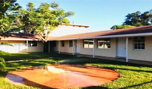 L-shaped exterior featuring a covered walkway, multi-pane windows, a central circular hardscape patio, and mature trees