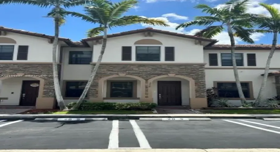 Two-story residence featuring a stucco facade with natural stone veneer accents, arched entryways, tile roof, and shuttered windows