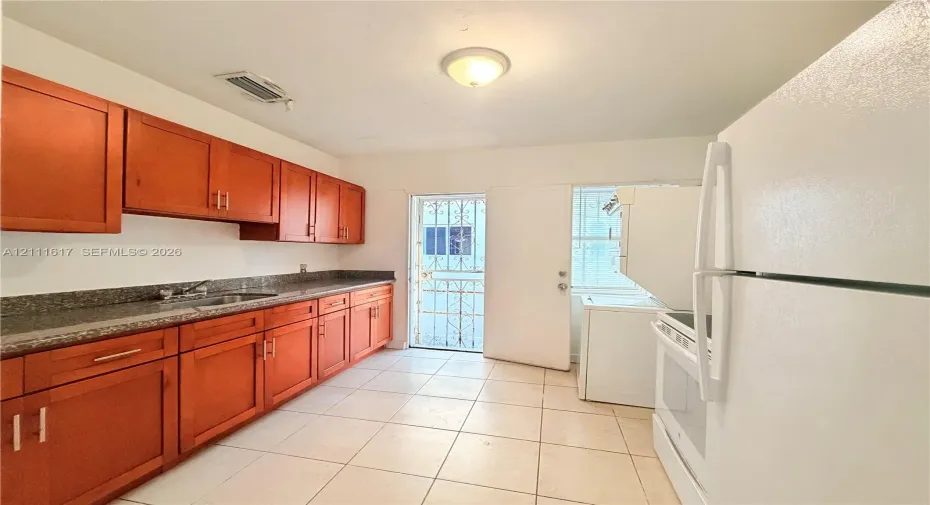 Kitchen featuring wood cabinetry, stone-finish countertops, stainless steel sink, tiled flooring, and exterior access via a metal security door