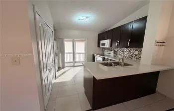 Kitchen featuring dark cabinetry, quartz countertops, mosaic tile backsplash, double-basin stainless steel sink with pull-down faucet, and tile flooring