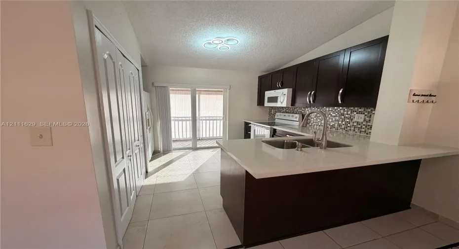 Kitchen featuring dark cabinetry, quartz countertops, mosaic tile backsplash, double-basin stainless steel sink with pull-down faucet, and tile flooring