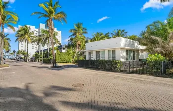 Single-story exterior featuring white stucco finish, flat roofline, metal perimeter fencing, and mature palm landscaping