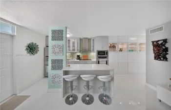 Kitchen featuring a central island with a quartz countertop, white cabinetry, integrated stainless steel appliances, a tile backsplash, and polished tile flooring. Lots of storage!