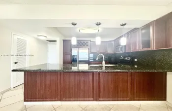 Kitchen featuring dark wood-finish cabinetry, built-in wine rack, stone-finish countertops, three pendant lights, and tile flooring