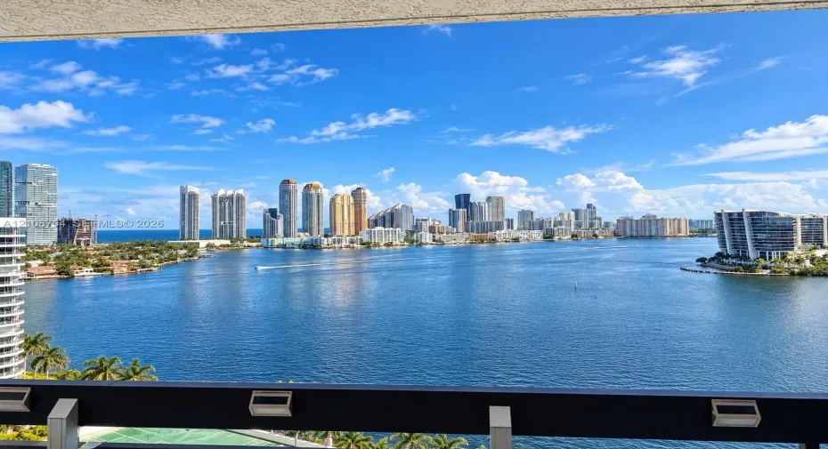 Outdoor balcony featuring a dark metal railing with integrated lighting, overlooking a wide expanse of water and a skyline