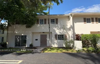 Two-story exterior featuring light-toned stucco facade, decorative window shutters, sliding glass door, and paver walkway