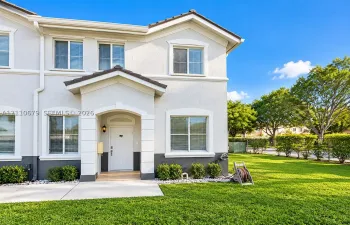 Stucco exterior featuring dual-tone paint, a covered entryway with stone-finish trim, multiple grid-pattern windows, and a paved walkway