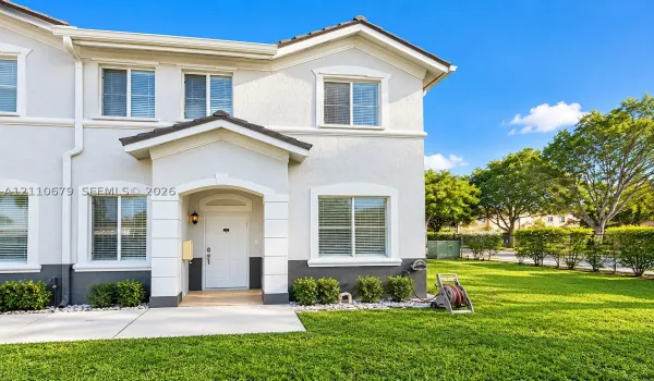 Stucco exterior featuring dual-tone paint, a covered entryway with stone-finish trim, multiple grid-pattern windows, and a paved walkway