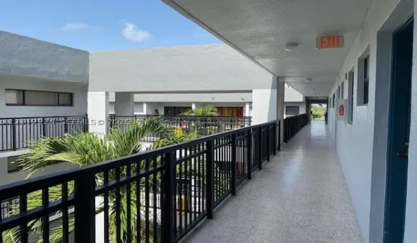 Open-air walkway featuring speckled concrete flooring, matte black metal railings, and stucco exterior walls