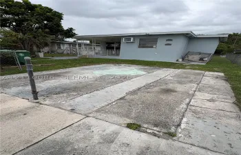 Concrete slab parking area with a covered patio, grass yard, and metal perimeter fencing