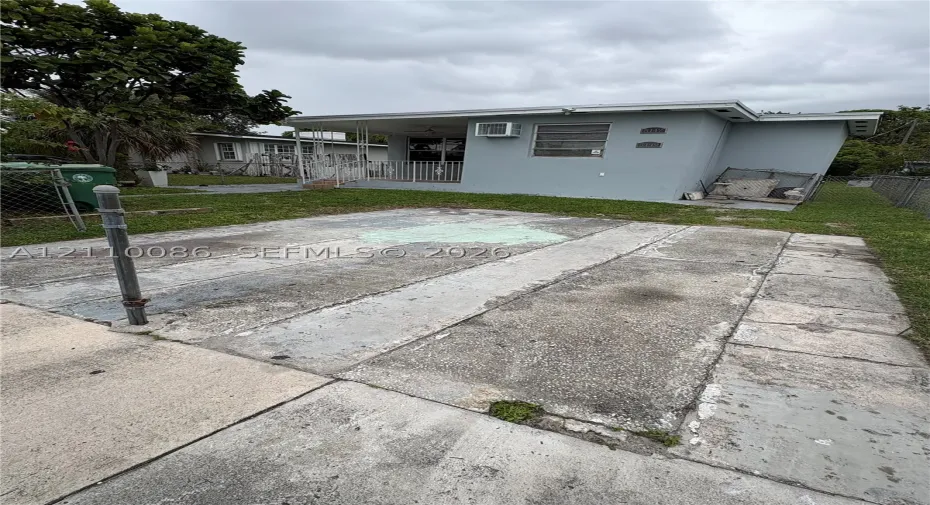 Concrete slab parking area with a covered patio, grass yard, and metal perimeter fencing
