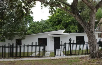 Single-story residence featuring a low-slope roofline, white exterior finish, dark-framed windows, and a black wrought-iron perimeter fence