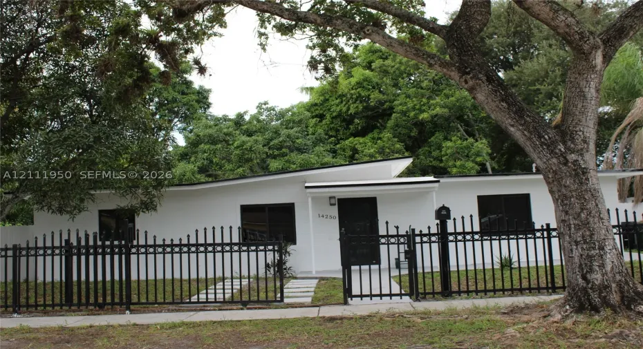 Single-story residence featuring a low-slope roofline, white exterior finish, dark-framed windows, and a black wrought-iron perimeter fence