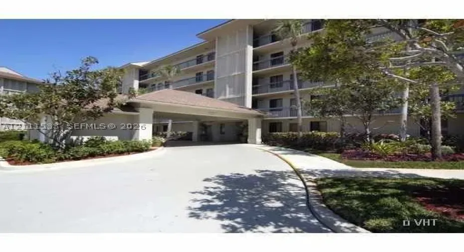 Multi-story building exterior featuring a covered porte-cochère, paved driveway, private balconies, and landscaped grounds
