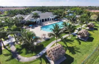 Community recreation area featuring a large swimming pool, concrete sun deck, and multiple thatched-roof gazebos set within a landscaped lawn