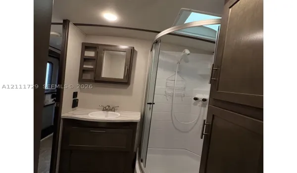 Bathroom featuring dark wood-finish cabinetry, a stone-pattern vanity countertop with an integrated basin, a curved glass-enclosed shower, a skylight, and wall-mounted medicine cabinet